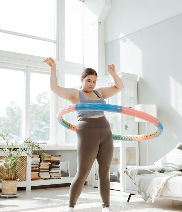 A woman in comfortable sportswear performing a fluid cardio movement in a bright, sunlit room.